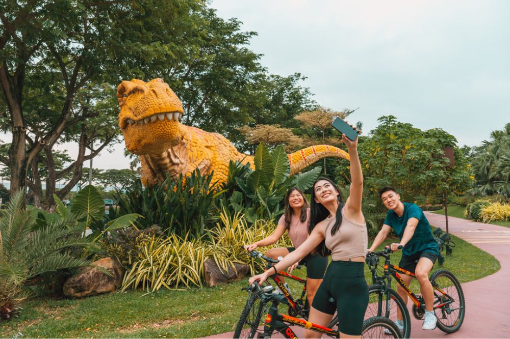a group of cyclists taking a selfie with a yellow dinosaur along changi airport's jurassic mile in singapore