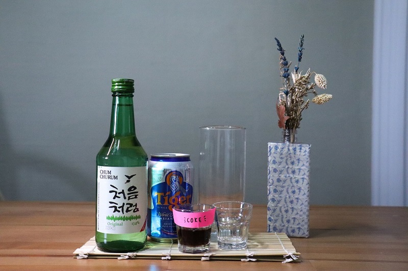 A bottle of original soju, beer, coke and cocktail glasses displayed on a table.