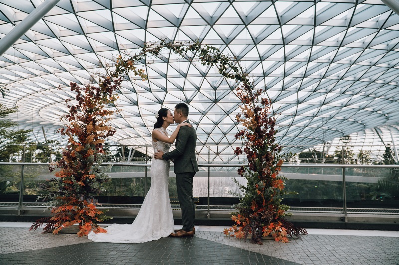 a couple exchanging vows in front of a flower arch against cloud9 piazza at jewel, best wedding venue in singapore