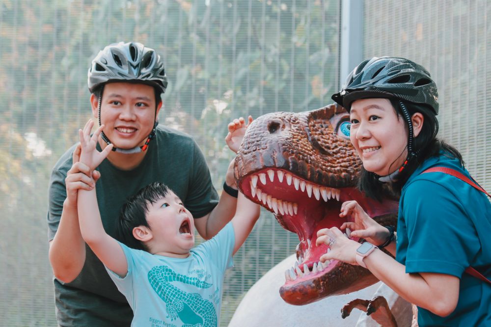 Family posing with dino displays along Jurassic Mile