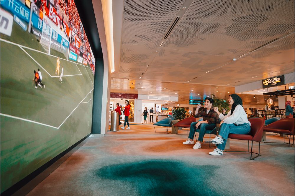 2 people sitting at the TV lounge watching a soccer match