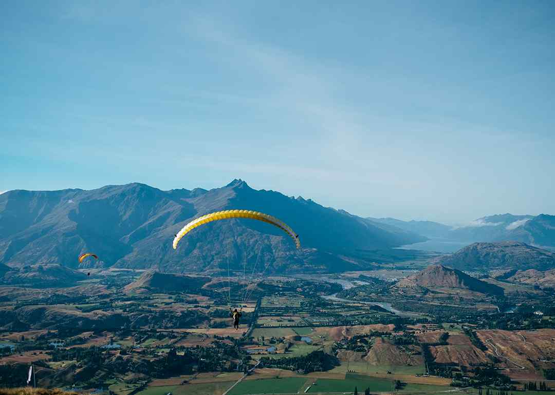 a paraglider above the vast landscape of coronet peak with views of the wakatipu basin, queenstown, new zealand