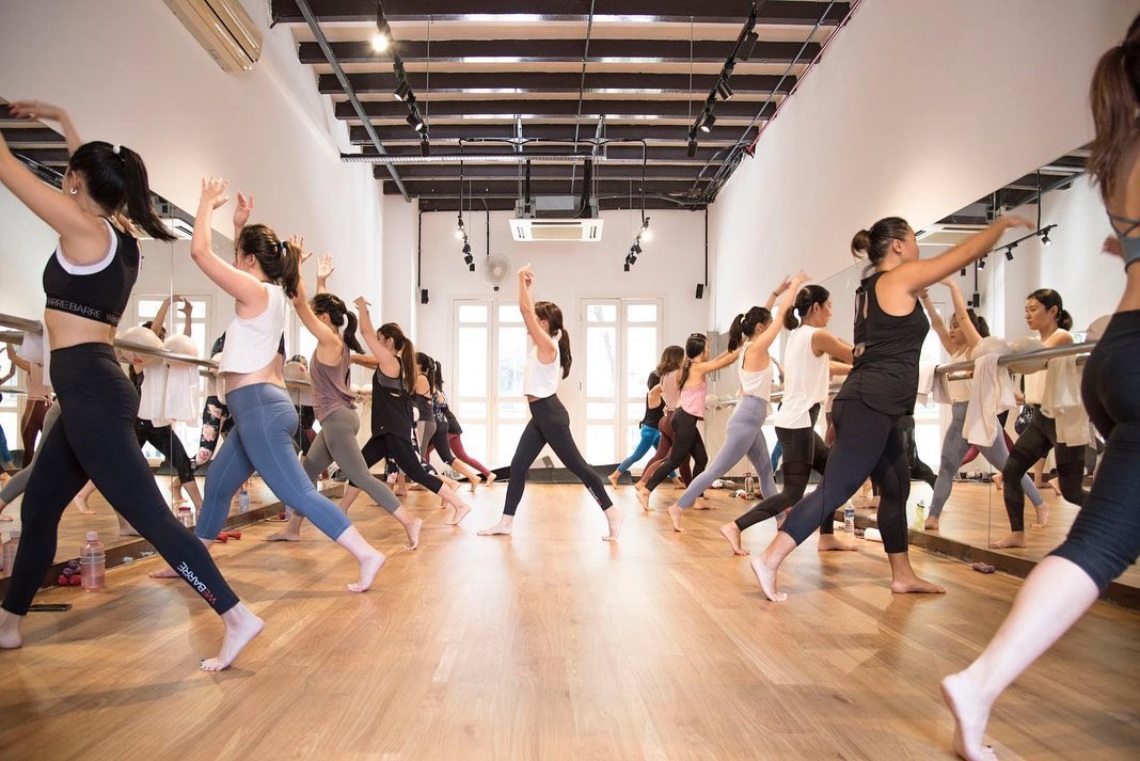 participants practice barre postures in two rows against mirrors at a dance studio in singapore