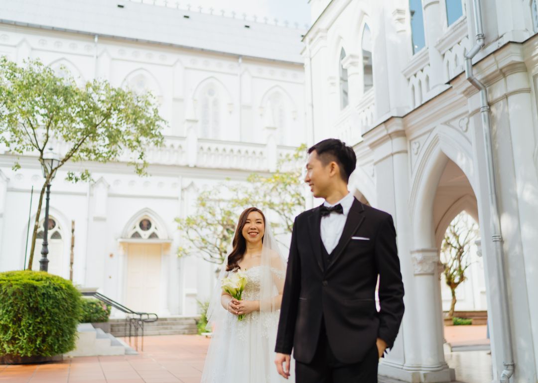 A wedding couple looks at each other, smiling in front of one of Chijmes’ cathedral facades.