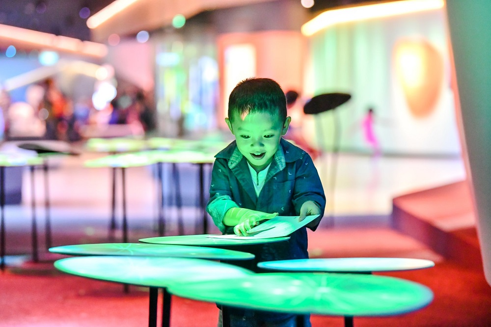 A boy smiling while playing with light displays at Changi Experience Studio