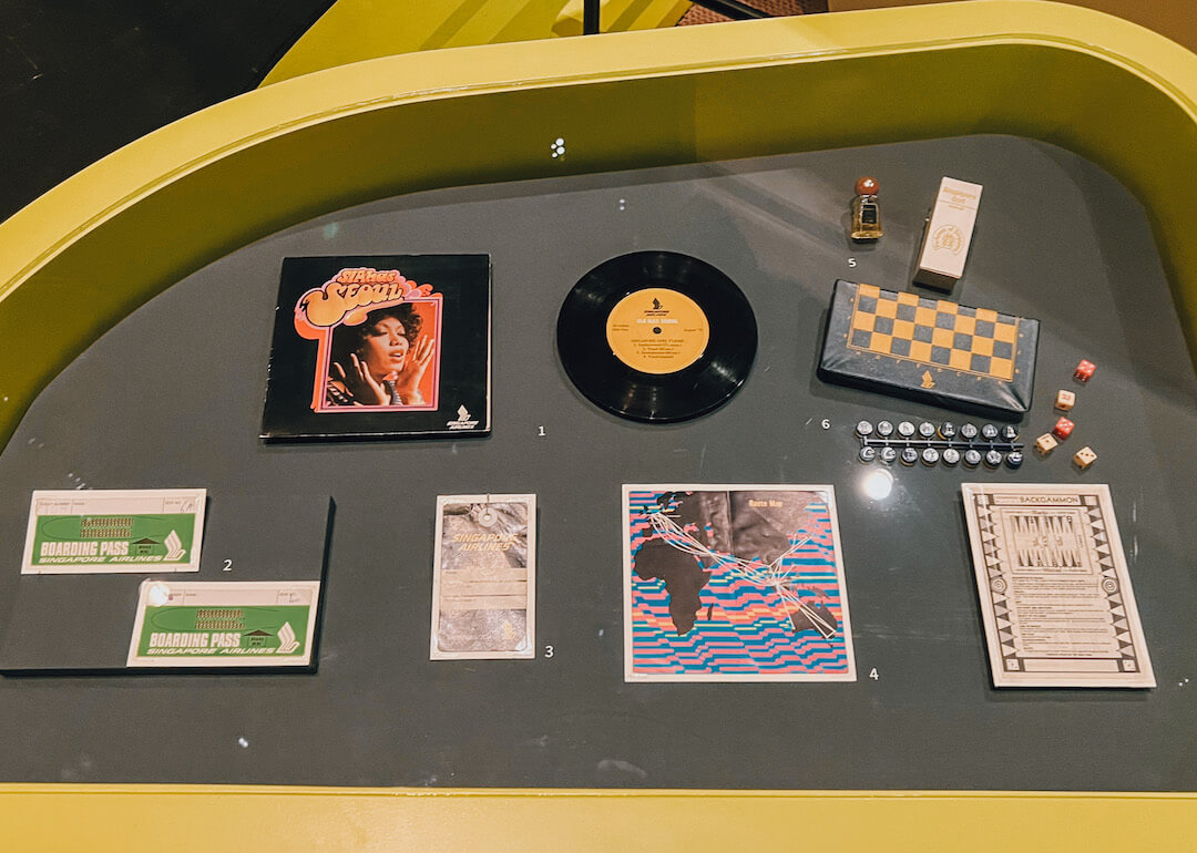 an array of vintage items, including a vinyl, singapore airlines inflight games, a perfume bottle and its packaging, singapore changi airport boarding passes and printed memorabilia at the national museum singapore travel exhibition